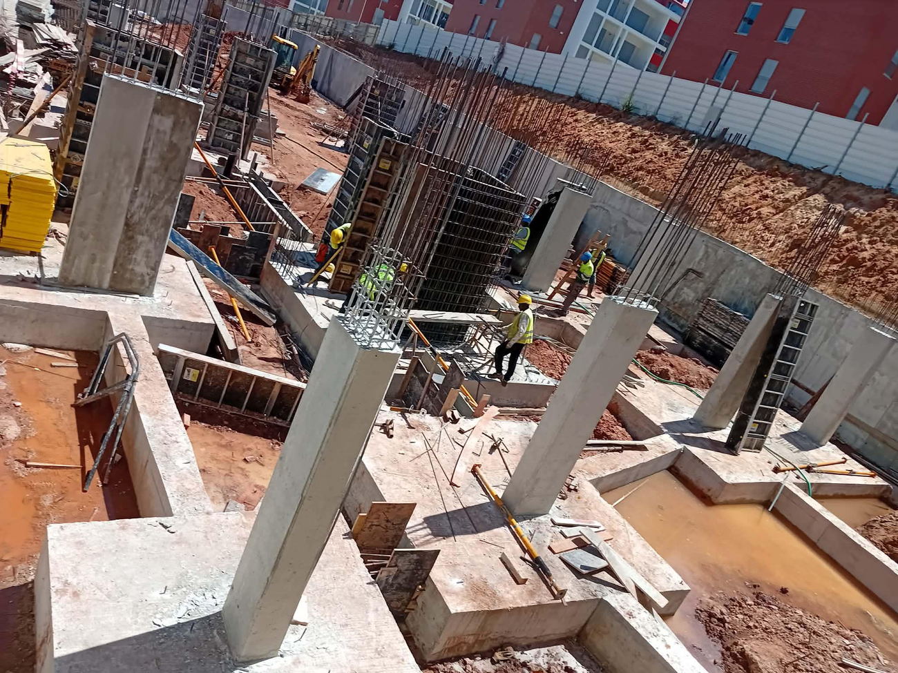 Vista aérea de uma obra, com sapatas, pilares em betão armado, cofragem e equipa em trabalho