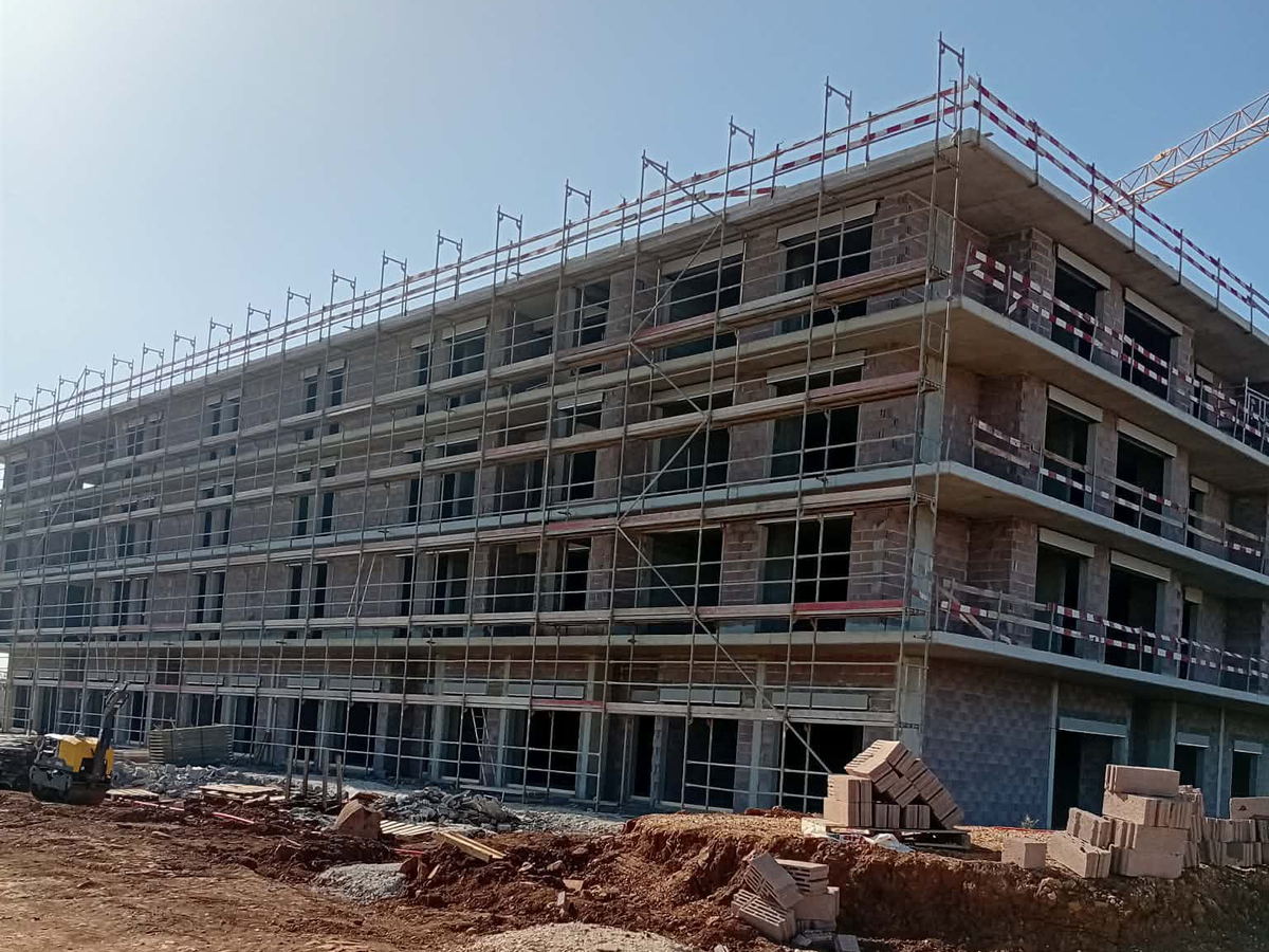 Edifício de quatro pisos com estrutura em betão armado, alvenarias em tijolo e andaime de fachada